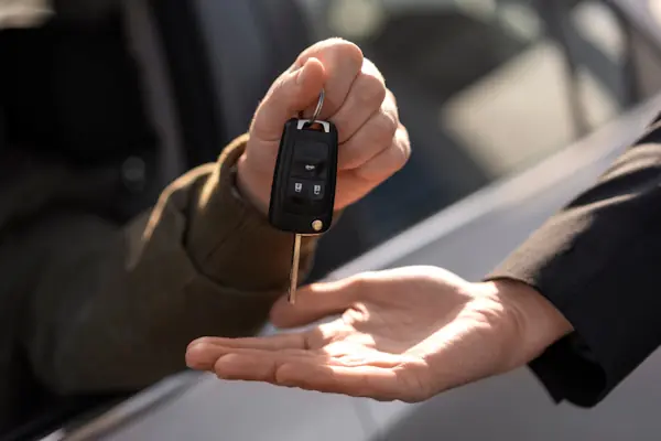 Fahrzeugschlüssel wird an der Autotür von Hand zu Hand übergeben